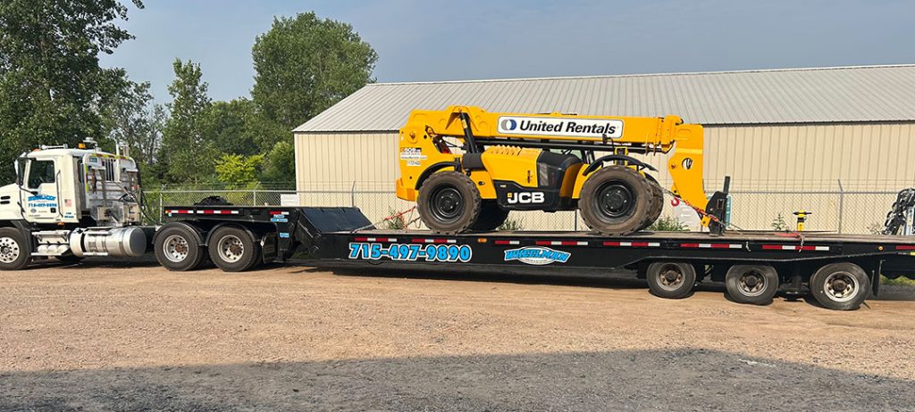 Wheelman Towing hauls a yellow JCB forklift on a flatbed trailer.