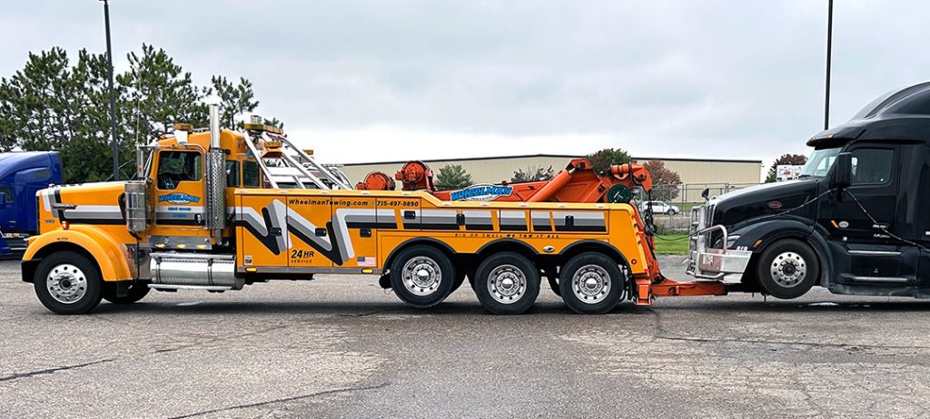 Wheelman Towing heavy wrecker towing a black semi‑truck in a parking lot.