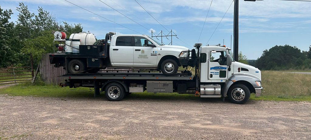 Wheelman Towing transports a white work truck on a flatbed tow truck.